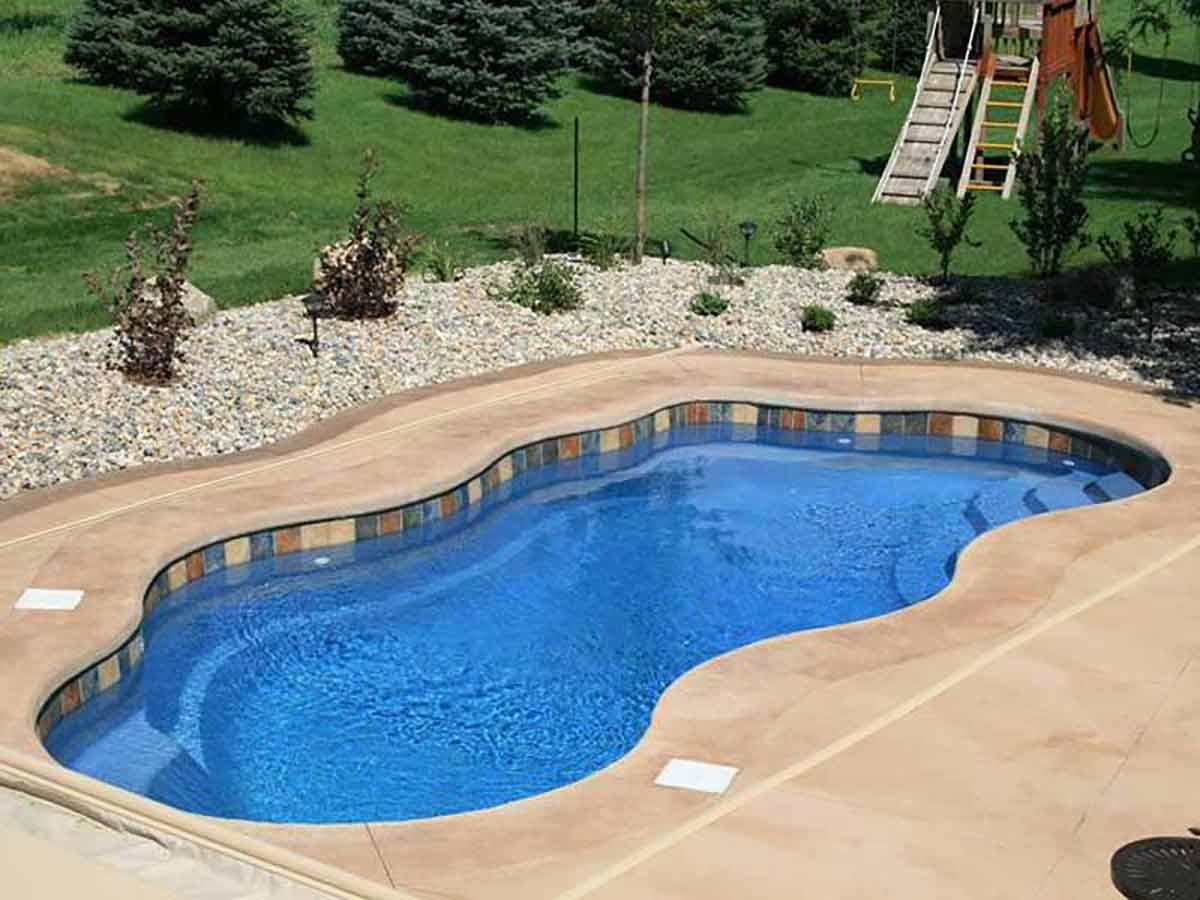 Freeform fiberglass pool with a mosaic tile waterline and a tan concrete deck